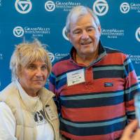 Two alumni getting their picture taken in front of the photo wall.